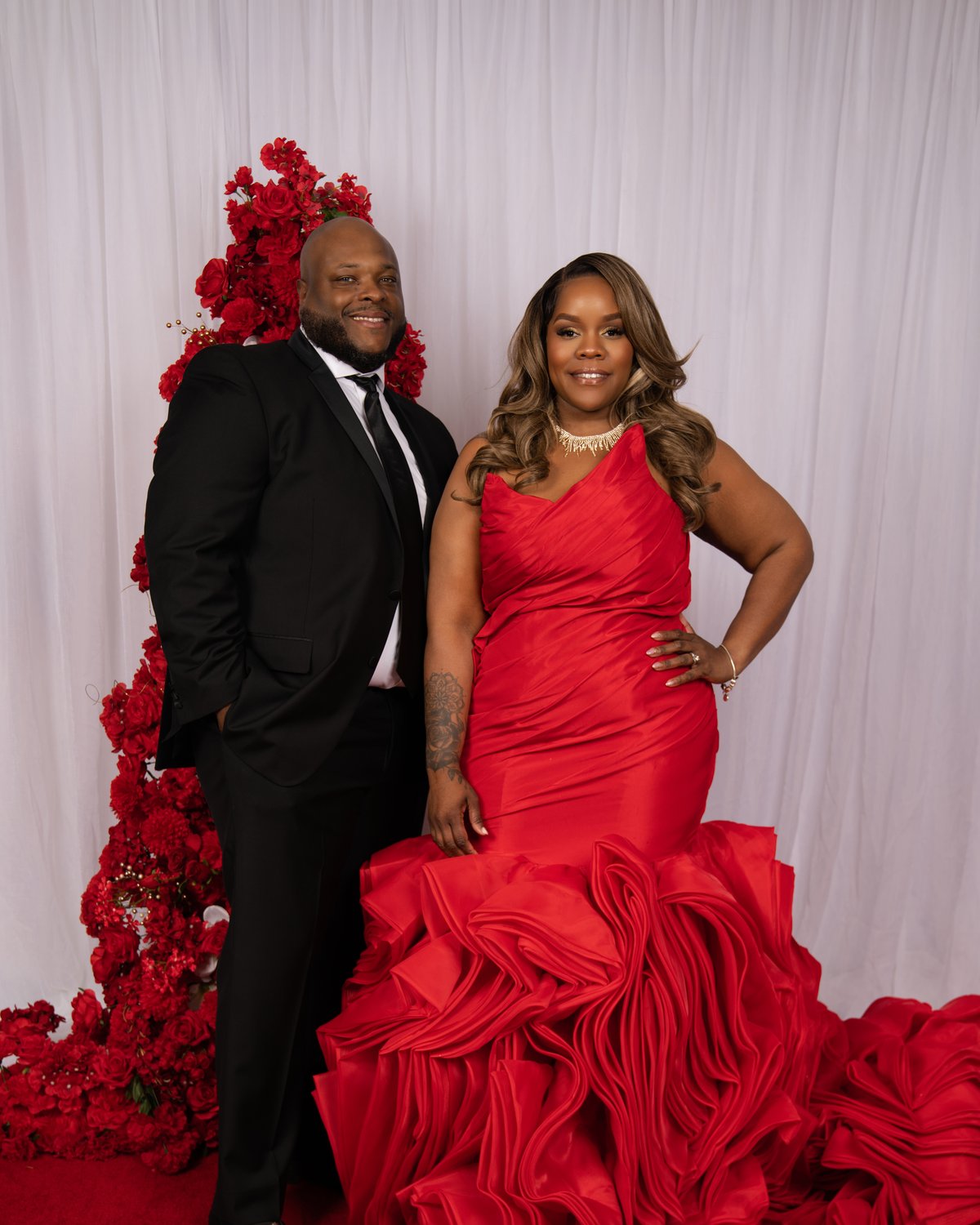 A couple in black tie and a red ruffled gown arriving on the Ruby Hollywood Glam carpet