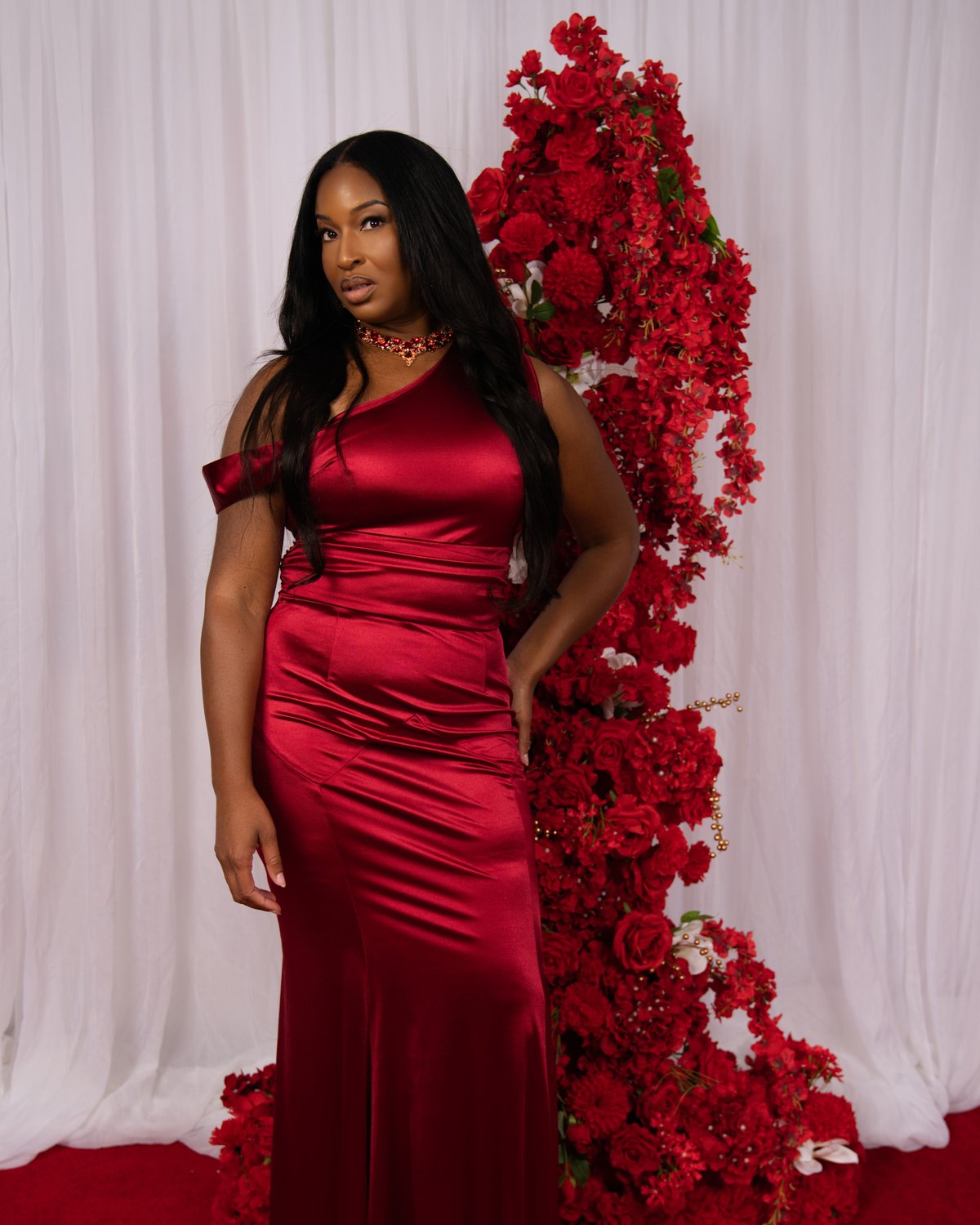 A guest in a red satin gown beside a wall of red roses on the Ruby Hollywood Glam carpet